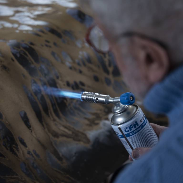 Arthur Unger zeichnet mithilfe eines Gasbrenners auf eine farbige Kupferplatte